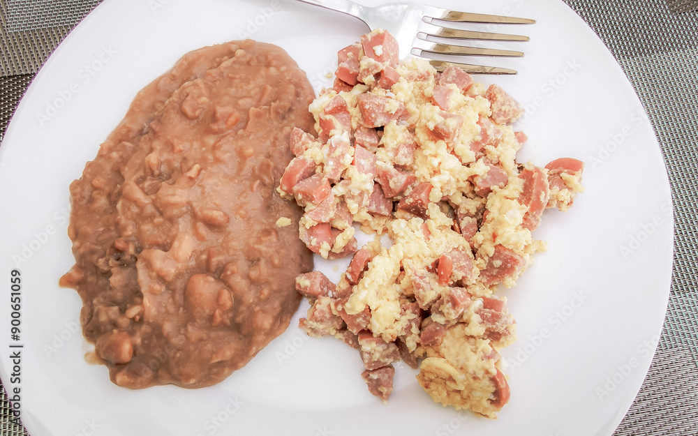 Breakfast scrambled eggs beans and bacon nicely arranged on plate.