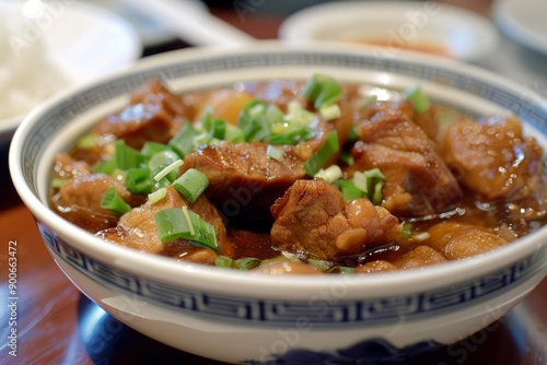 Closeup of a flavorful bowl of asianstyle braised pork belly topped with fresh green onions