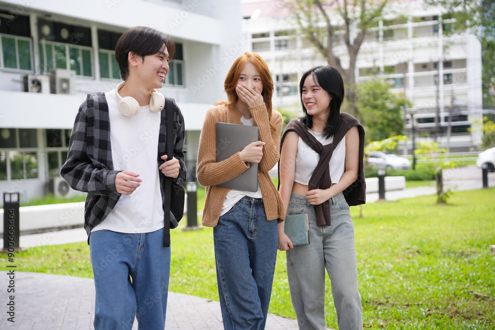 Obraz premium Group of three asian students are walking and laughing together on a university campus, enjoying their time spent together