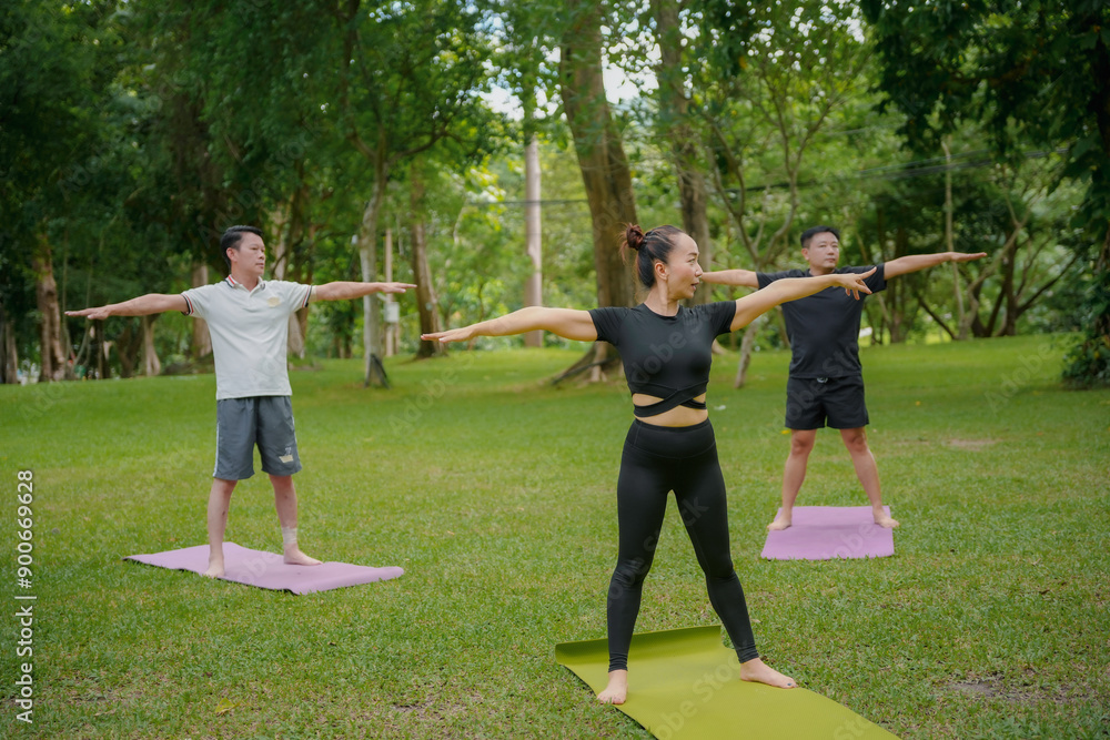 Diverse group practices yoga in a lush park, guided by an instructor. Men and women of asian descent wear sportswear, engaging in poses. Surrounding greenery enhances their balance and harmony Diverse group practices yoga in a lush park, guided by an instructor. Men and women of asian descent wear sportswear, engaging in poses. Surrounding greenery enhances their balance and harmony