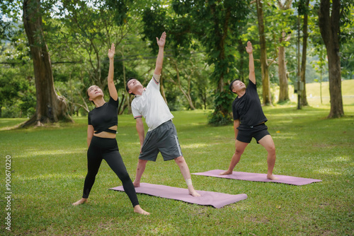 Three asian people doing yoga in the park, standing on their mats and stretching their bodies during a sunny day © amnaj