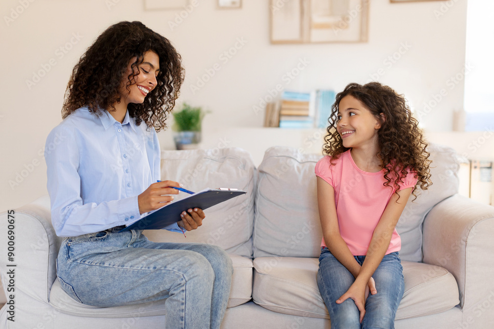 Friendly female psychologist with clipboard communicating with little child girl during therapy session, kid sharing her thoughts with therapist Friendly female psychologist with clipboard communicating with little child girl during therapy session, kid sharing her thoughts with therapist
