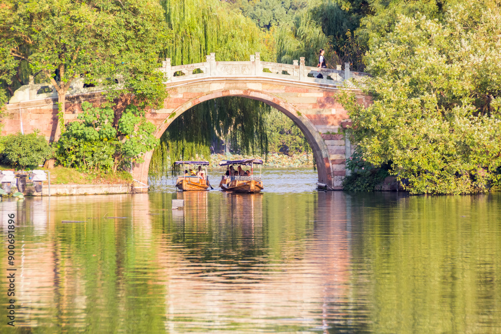 Boats passing under a moon bridge in Quyuan garden at West lake in Hangzhou, China