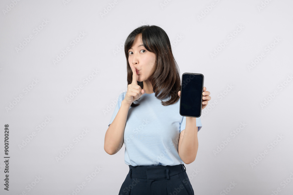 Beware of online theft Young Asian woman in her 30s wearing a blue t-shirt and jeans. Holding a cell phone while making a shush gesture with the other hand worried expression Beware of online theft Young Asian woman in her 30s wearing a blue t-shirt and jeans. Holding a cell phone while making a shush gesture with the other hand worried expression