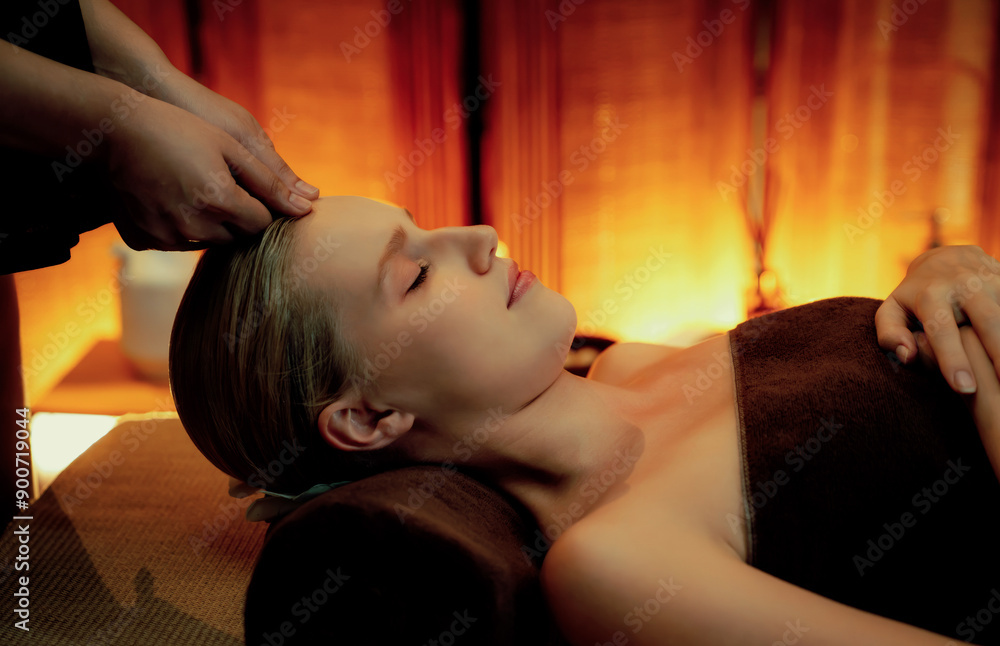 Obraz premium Caucasian woman enjoying relaxing anti-stress head massage and pampering facial beauty skin recreation leisure in warm candle lighting ambient salon spa in luxury resort or hotel. Quiescent