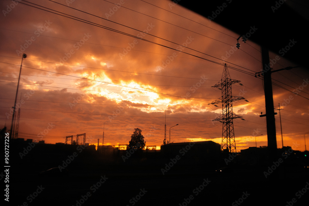 Fototapeta premium The view from the train window at sunset, with the power line and silhouetted city houses. The journey is taking place in the evening.