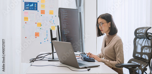 Young adult Asian female software developer coding program on desktop computer. Woman work from home, remote working, freelance programmer job, smart digital nomad lifestyle concept