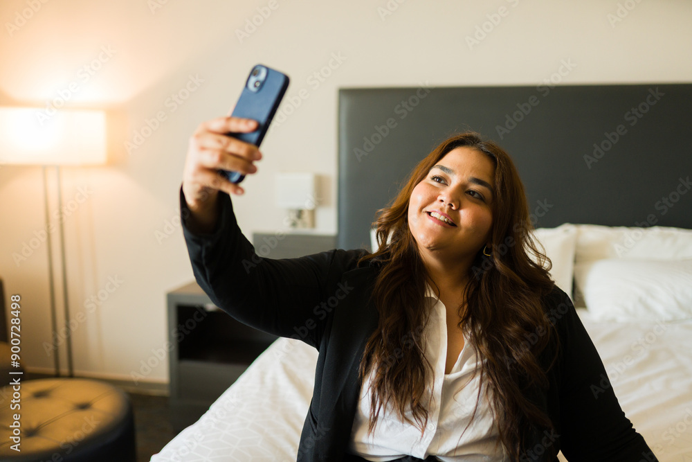 Happy female entrepreneur captures a selfie with her phone while relaxing on a hotel room bed Happy female entrepreneur captures a selfie with her phone while relaxing on a hotel room bed