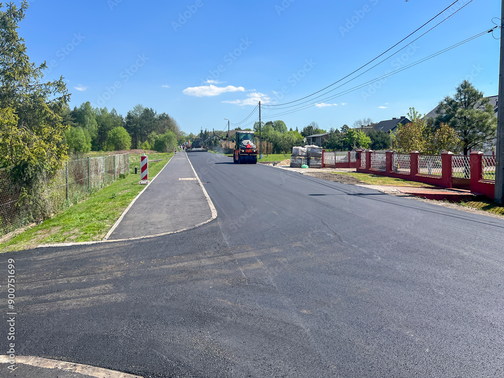 Fototapeta premium Laying the last layer of asphalt on the modernized road and sidewalk. Operation of a machine for laying asphalt and road rollers