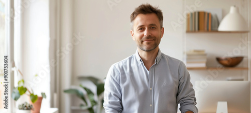 A portrait of a happy man standing in a modern home office, looking at the camera and smiling