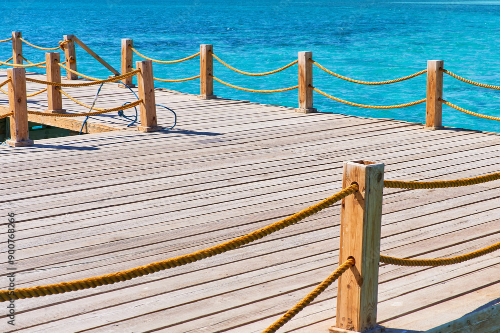 Fototapeta premium Marine wooden dock with yellow ropes and blue clear water
