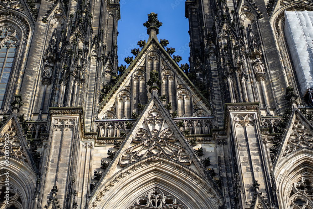 Fototapeta premium Intricate architectural details of a Gothic cathedral facade under a bright blue sky.