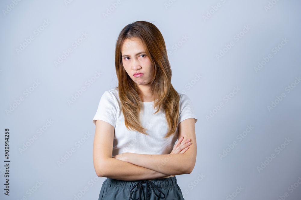 A young woman with an upset facial expression, standing with her arms crossed against a white background, conveying displeasure or frustration. A young woman with an upset facial expression, standing with her arms crossed against a white background, conveying displeasure or frustration.