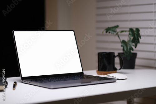 Laptop and office supplies on white table in modern dark home office at night.