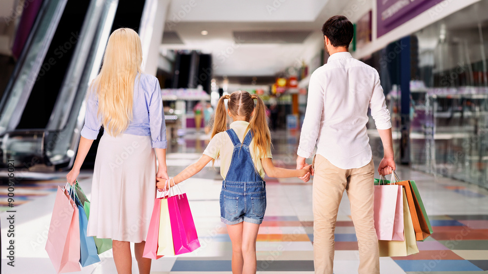 A family, consisting of a mother, father, and young daughter, is walking through a modern mall. The family is carrying multiple colorful shopping bags, suggesting they have been shopping. A family, consisting of a mother, father, and young daughter, is walking through a modern mall. The family is carrying multiple colorful shopping bags, suggesting they have been shopping.