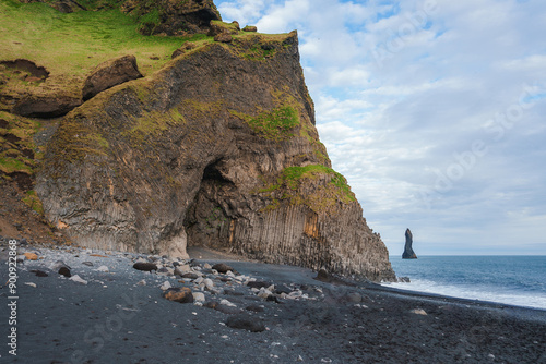 A stunning coastal scene at Reynisfjara black sand beach in Iceland, featuring rugged cliffs with basalt columns and the dramatic Reynisdrangar sea stacks. photo