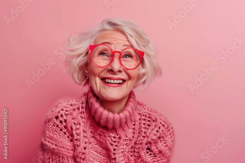 Happy smiling senior woman wearing sunglasses, pink solid colorful background, space for text / Femme âgée souriante et heureuse avec lunettes de soleil, fond rose, espace pour le texte