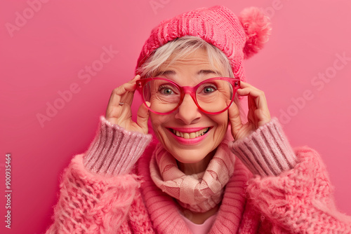 Happy smiling senior woman wearing sunglasses, pink solid colorful background, space for text / Femme âgée souriante et heureuse avec lunettes de soleil, fond rose, espace pour le texte