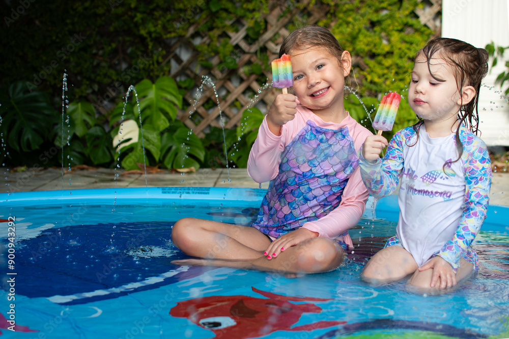 Two cute Caucasian children eating rainbow popsicle in a pool. Kids ...