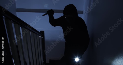 A thief in a black cloak and gloves sneaks into a house at midnight, holding a knife and flashlight, with the intent to harm the occupants.