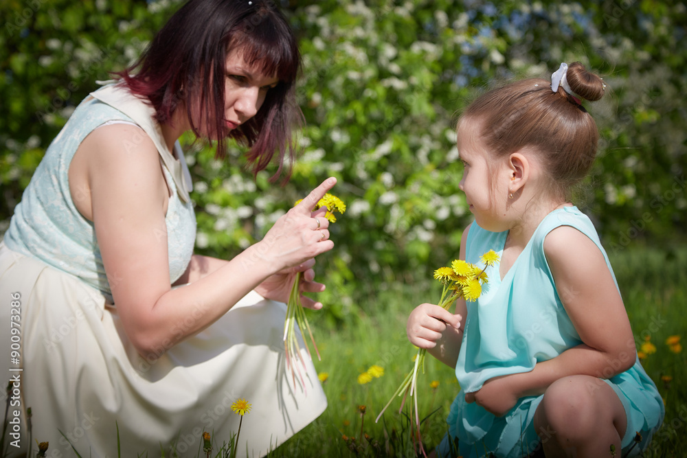 Happy mother and daughter enjoying rest, playing and fun on nature on a green lawn with dandelions and blooming apple tree on the background. Woman and girl resting outdoors in summer and spring day Happy mother and daughter enjoying rest, playing and fun on nature on a green lawn with dandelions and blooming apple tree on the background. Woman and girl resting outdoors in summer and spring day