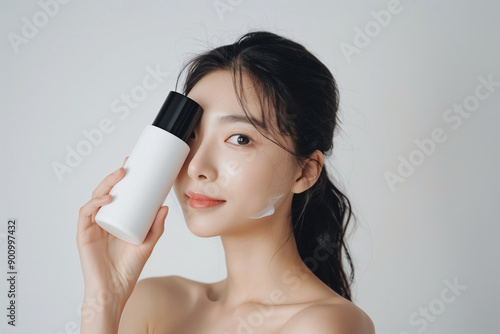 Close-Up of South Korean Glowing Skin Model Holding White Skin Cream Bottle with Black Lid Against White Background