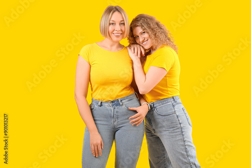 Beautiful happy women in stylish jeans on yellow background © Pixel-Shot