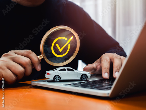 Looking for new car on website, buying and selling, search engine online concept. Yellow checkmark in magnifying glass lens holding by people who using laptop computer with white car toy on table. photo