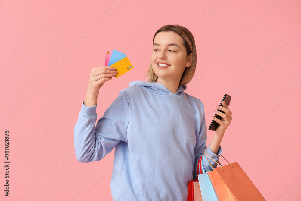 Young woman with credit cards, mobile phone and shopping bags on pink background Young woman with credit cards, mobile phone and shopping bags on pink background