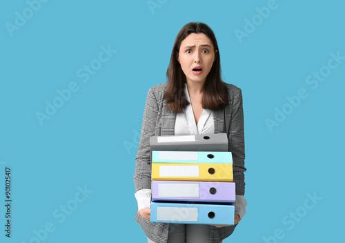 Shocked young businesswoman with folders on blue background