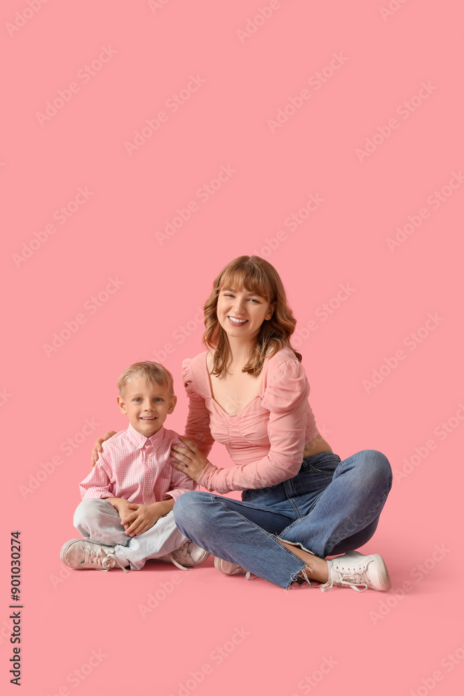 Happy mother and her little son sitting on pink background Happy mother and her little son sitting on pink background