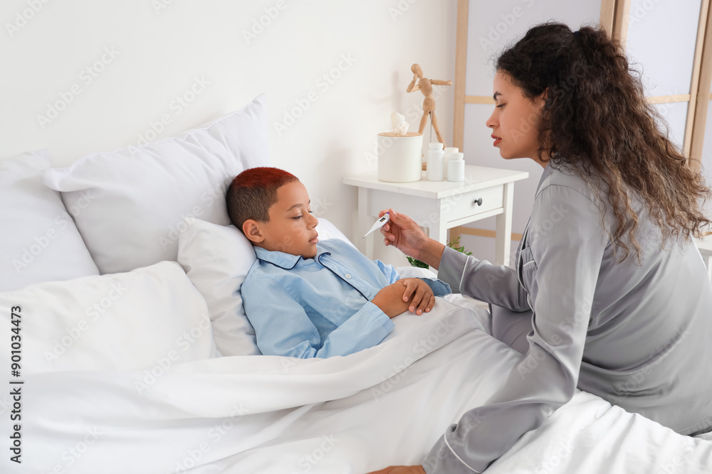 Sick little African-American boy and his mother with thermometer lying in bedroom Sick little African-American boy and his mother with thermometer lying in bedroom