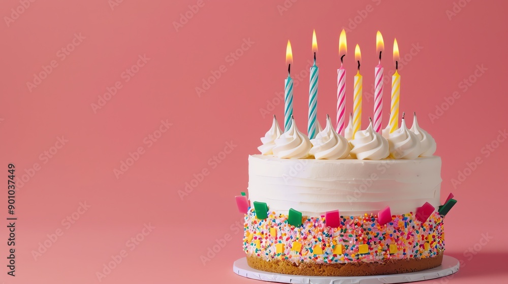 A birthday cake with lit candles and colorful sprinkles on a pink background. A birthday cake with lit candles and colorful sprinkles on a pink background.