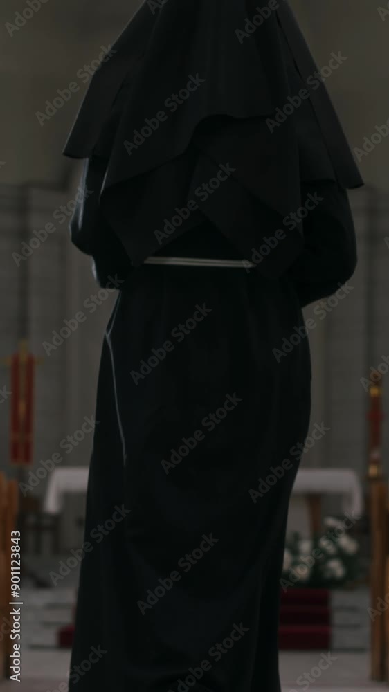 Vertical tilt up back view of religious sister in black clothes walking to altar along aisle in church Vertical tilt up back view of religious sister in black clothes walking to altar along aisle in church