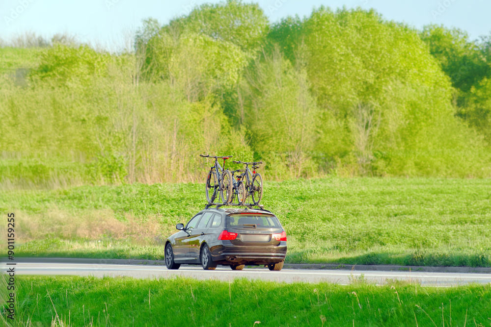 Fototapeta premium Family car with mountain bikes on roof rack driving on a sunny country road