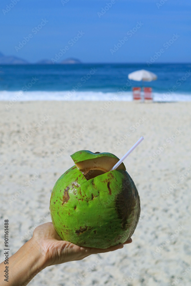 Fresh young coconut in hand with sandy beach of Copacabana, Rio de Janeiro, Brazil, South America in the backdrop Fresh young coconut in hand with sandy beach of Copacabana, Rio de Janeiro, Brazil, South America in the backdrop