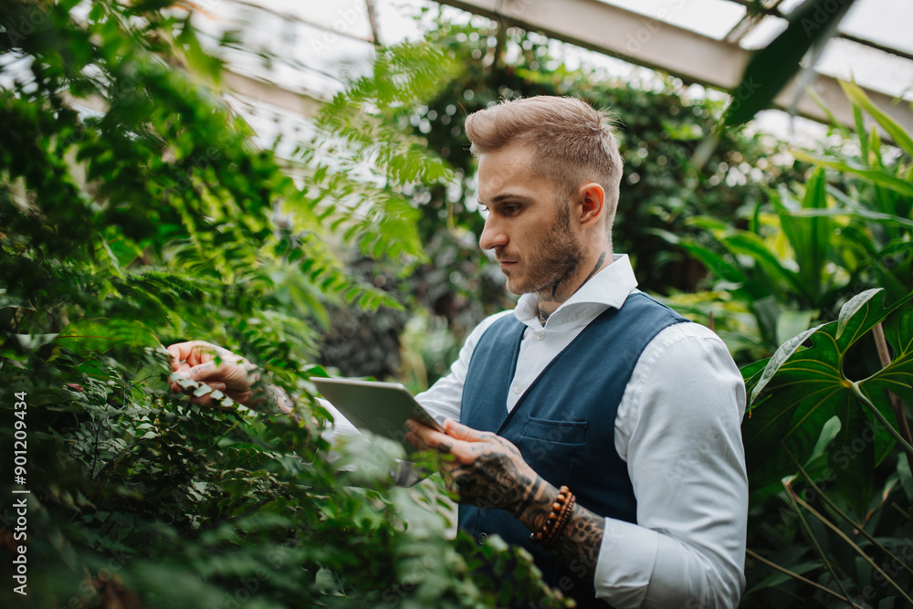 Handsome businessman with tablet, standing in botanical garden, in the middle of lush green foliage, looking at camera. Concept of business corporate social responsibility and ESG. Handsome businessman with tablet, standing in botanical garden, in the middle of lush green foliage, looking at camera. Concept of business corporate social responsibility and ESG.