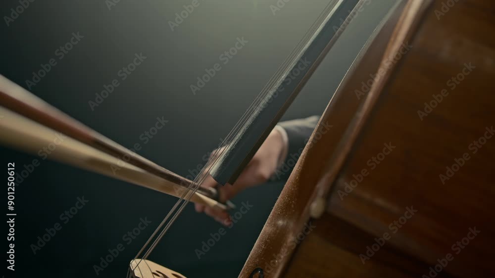 Closeup of graceful hand of unrecognizable classical musician holding bow playing cello on black background Closeup of graceful hand of unrecognizable classical musician holding bow playing cello on black background