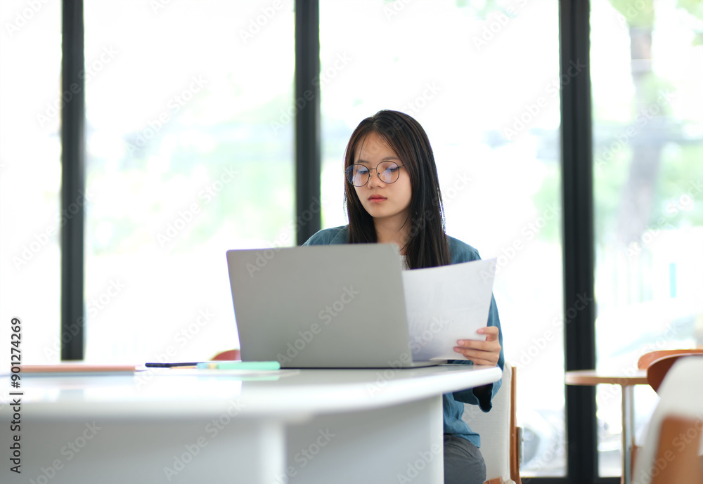 A woman is sitting at a table with a laptop and a piece of paper A woman is sitting at a table with a laptop and a piece of paper