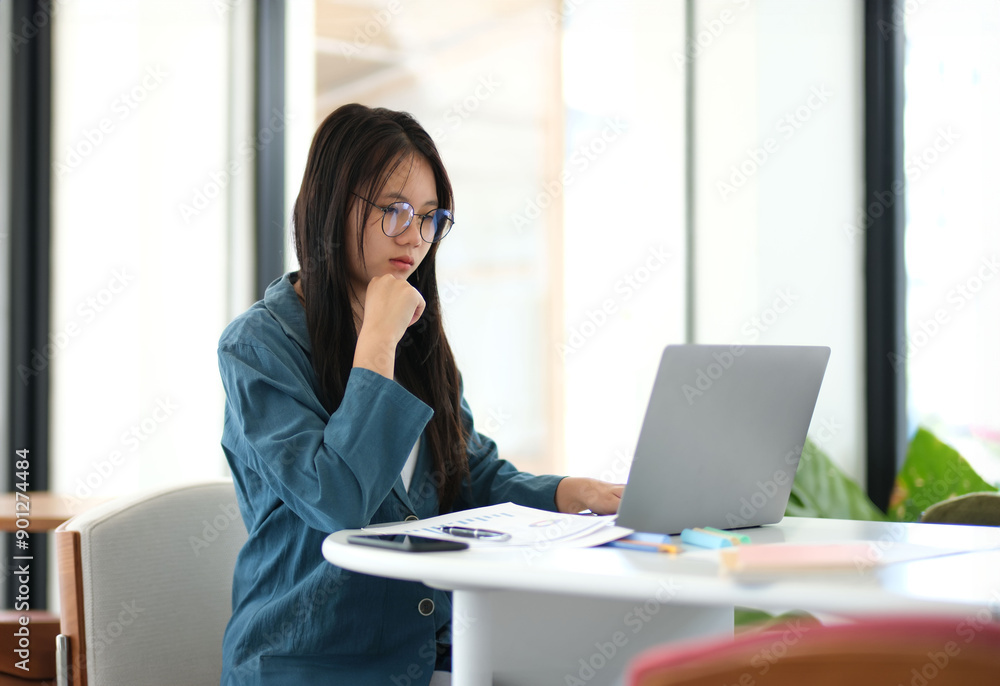 A woman is sitting at a desk with a laptop open in front of her A woman is sitting at a desk with a laptop open in front of her