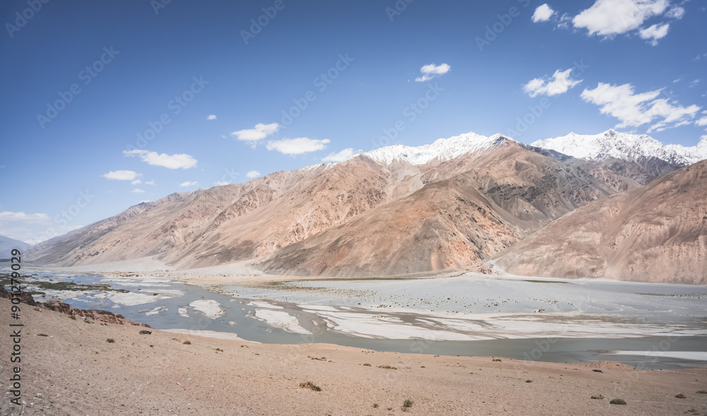 Pyanj River flows in Wakhan Valley among rocky high mountains against snow-capped peaks and glaciers in Tajikistan's Tien Shan mountains, landscape for background Pyanj River flows in Wakhan Valley among rocky high mountains against snow-capped peaks and glaciers in Tajikistan's Tien Shan mountains, landscape for background