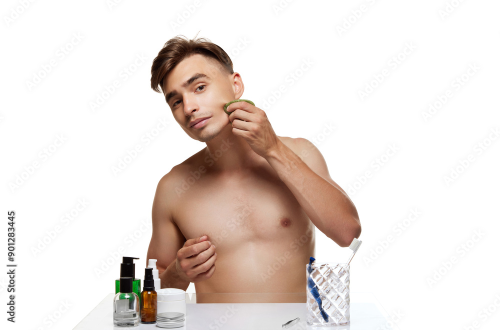 Young man looking at camera as mirror and doing facial massage in bathroom against white studio background. Treatment. Concept of beauty, care, cosmetology, wellness, masculinity. Ad Young man looking at camera as mirror and doing facial massage in bathroom against white studio background. Treatment. Concept of beauty, care, cosmetology, wellness, masculinity. Ad