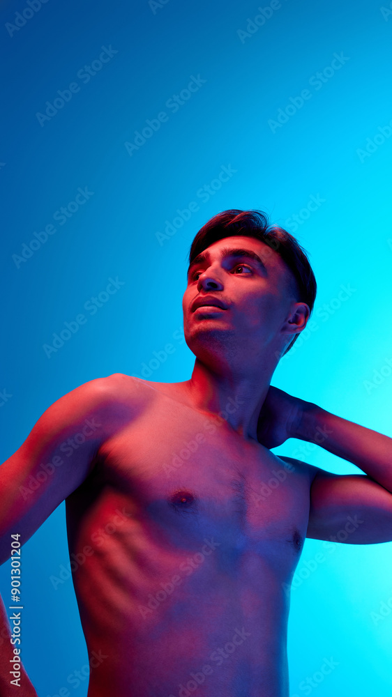 Shirtless man posing looks upward with thoughtful expression with hand resting on neck in neon light against blue gradient background. Concept of beauty, care, cosmetology, wellness, masculinity. Ad Shirtless man posing looks upward with thoughtful expression with hand resting on neck in neon light against blue gradient background. Concept of beauty, care, cosmetology, wellness, masculinity. Ad