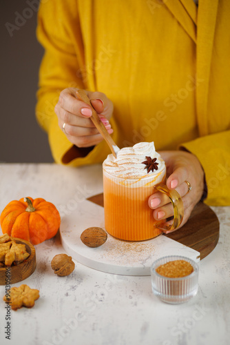 Woman holding cup of pumpkin spice latte with whipped cream at yellow background. Close up. Vertical