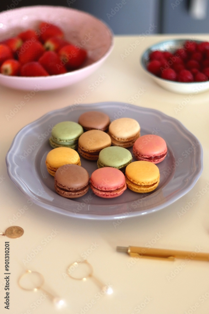 Plate of pastel macarons, cookies and chocolate, cup of tea of coffee, glass of bubble water, various berries, books and accessories on the table. Selective focus, pastel colors. Plate of pastel macarons, cookies and chocolate, cup of tea of coffee, glass of bubble water, various berries, books and accessories on the table. Selective focus, pastel colors.