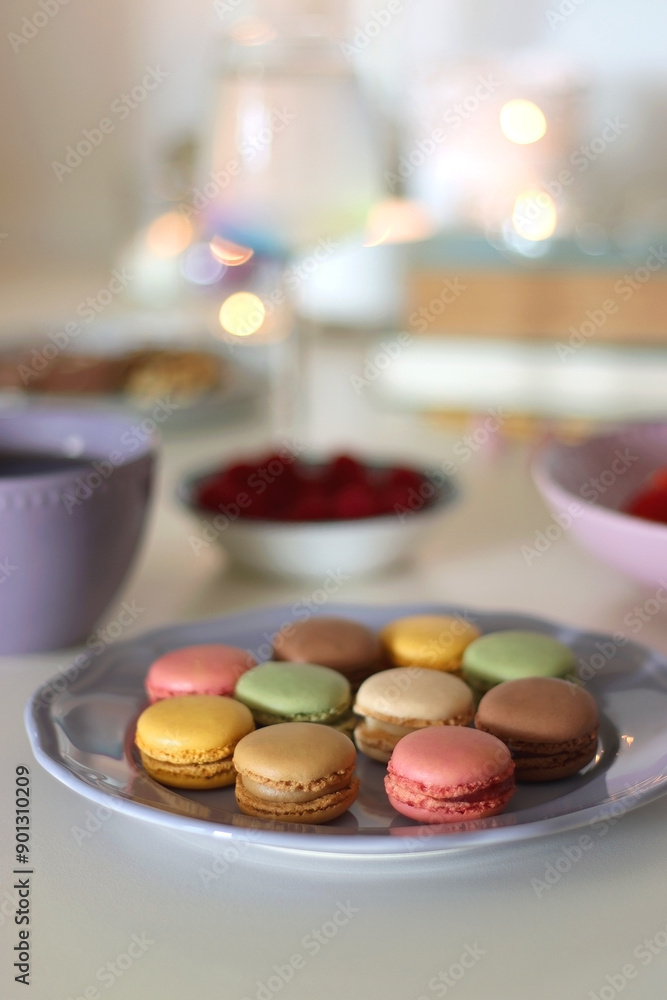 Plate of pastel macarons, cookies and chocolate, cup of tea of coffee, glass of bubble water, various berries, books and accessories on the table. Selective focus, pastel colors. Plate of pastel macarons, cookies and chocolate, cup of tea of coffee, glass of bubble water, various berries, books and accessories on the table. Selective focus, pastel colors.
