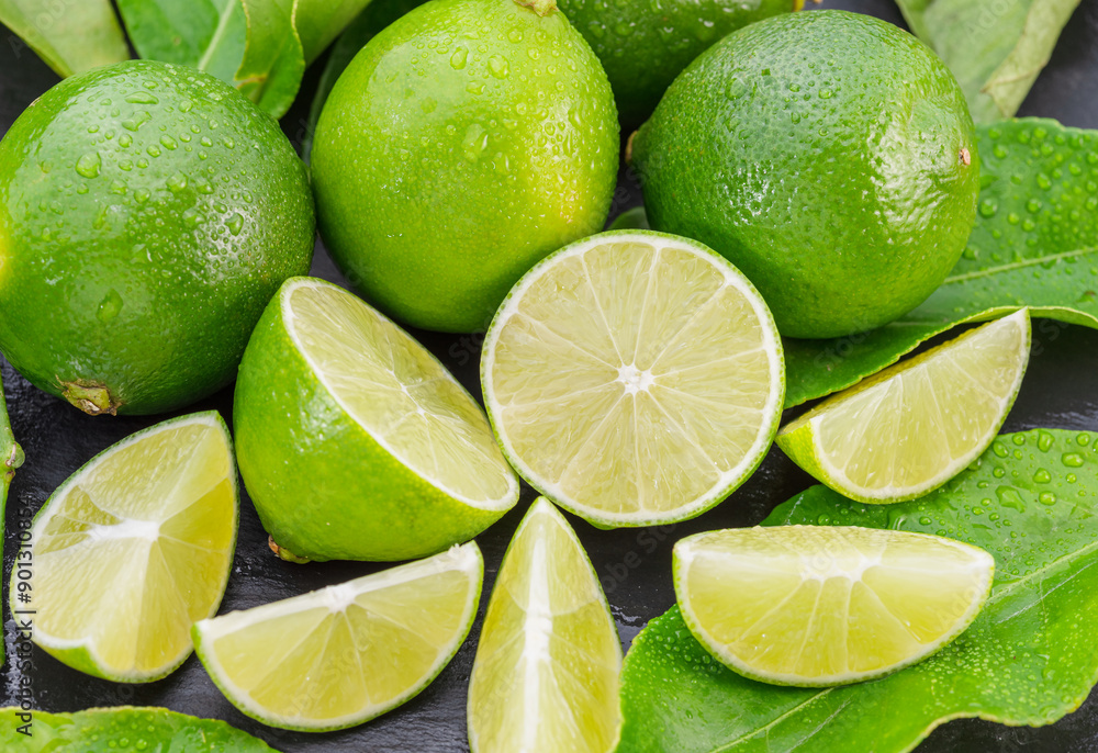 Ripe lime fruits with slices and lime leaves on a gray stone table. Ripe lime fruits with slices and lime leaves on a gray stone table.