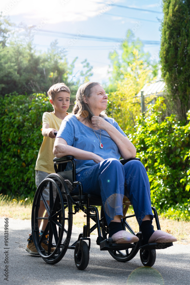 Boy carrying his grandmother in a wheelchair for a walk outdoors Boy carrying his grandmother in a wheelchair for a walk outdoors