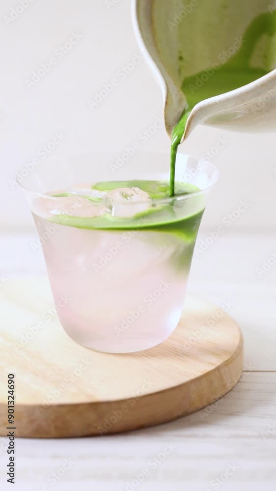 Pouring matcha drink into pink coconut water presented in multiple layers with rock ice. Green tea drink with ice. Closeup. Pouring matcha drink into pink coconut water presented in multiple layers with rock ice. Green tea drink with ice. Closeup.