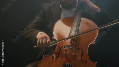 Cropped shot of handsome male cellist in suit sitting on chair while playing cello on black background